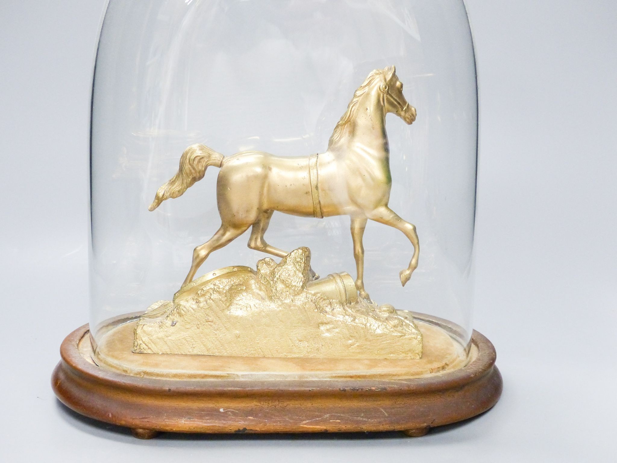 A Victorian gilt metal model of a horse with trophies of war to the base, under a glass dome, total height 30 cm